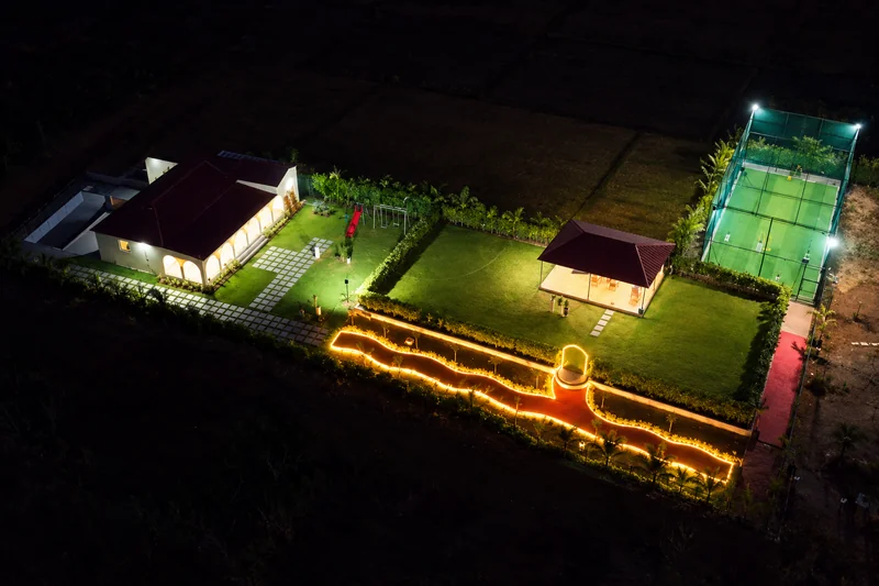 Night aerial view of illuminated residence, lawn, pavilion and cricket turf — AI recreation from supplied reference