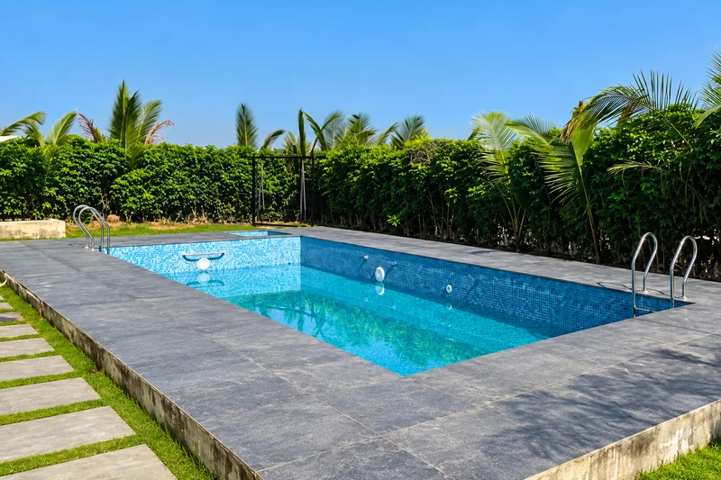Blue swimming pool edged by paving, palms and green hedges — AI recreation from supplied reference